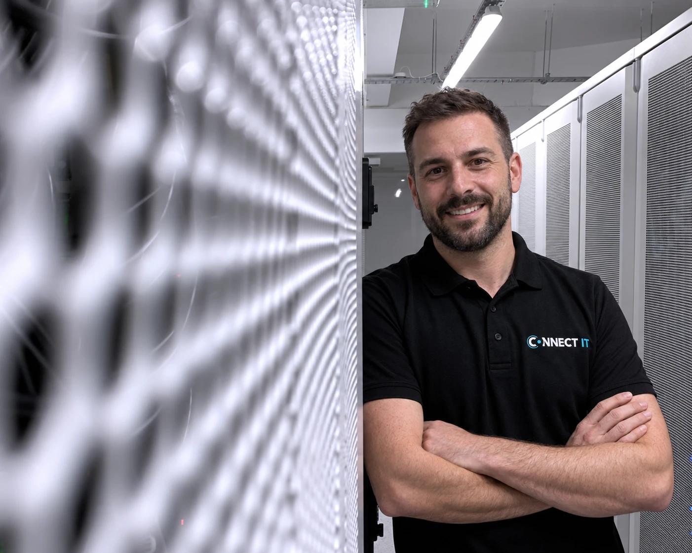 Lachende Connect IT-engineer met de armen over elkaar tussen de serverracks in het datacenter
